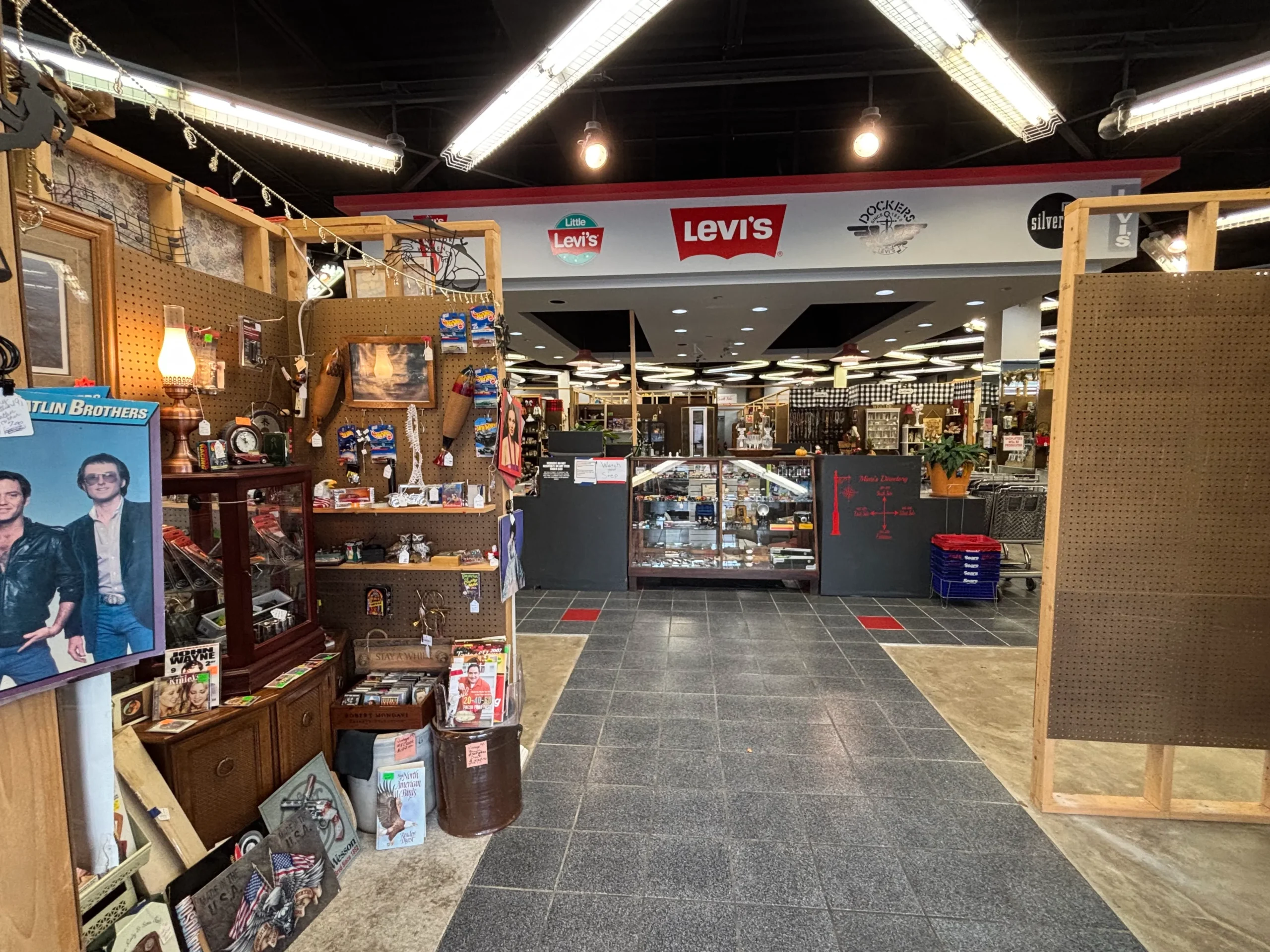 A vintage shop interior filled with memorabilia, clothing, and collectibles, featuring wooden displays and a glass showcase